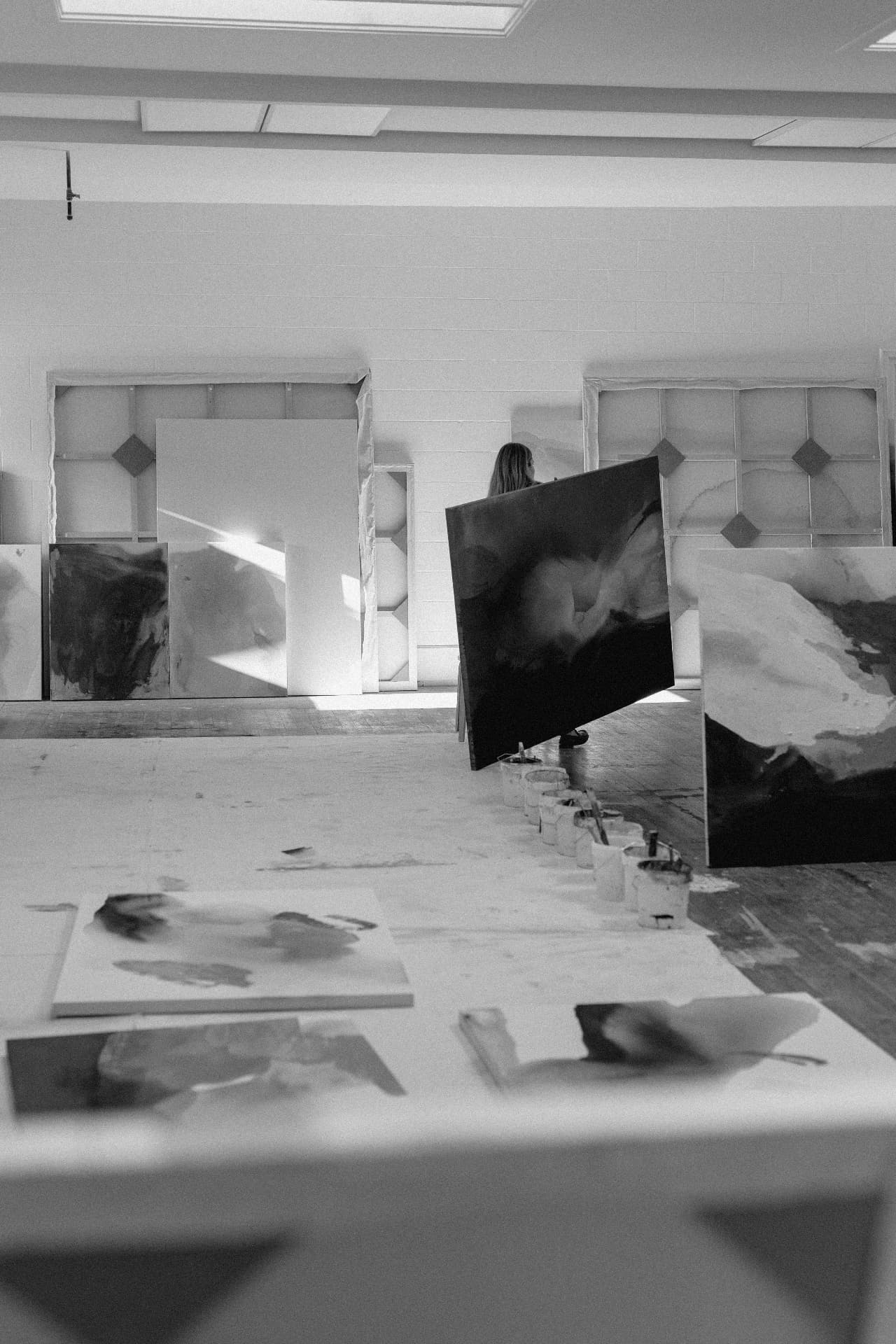 joy kinna carrying a dark abstract painting through her studio