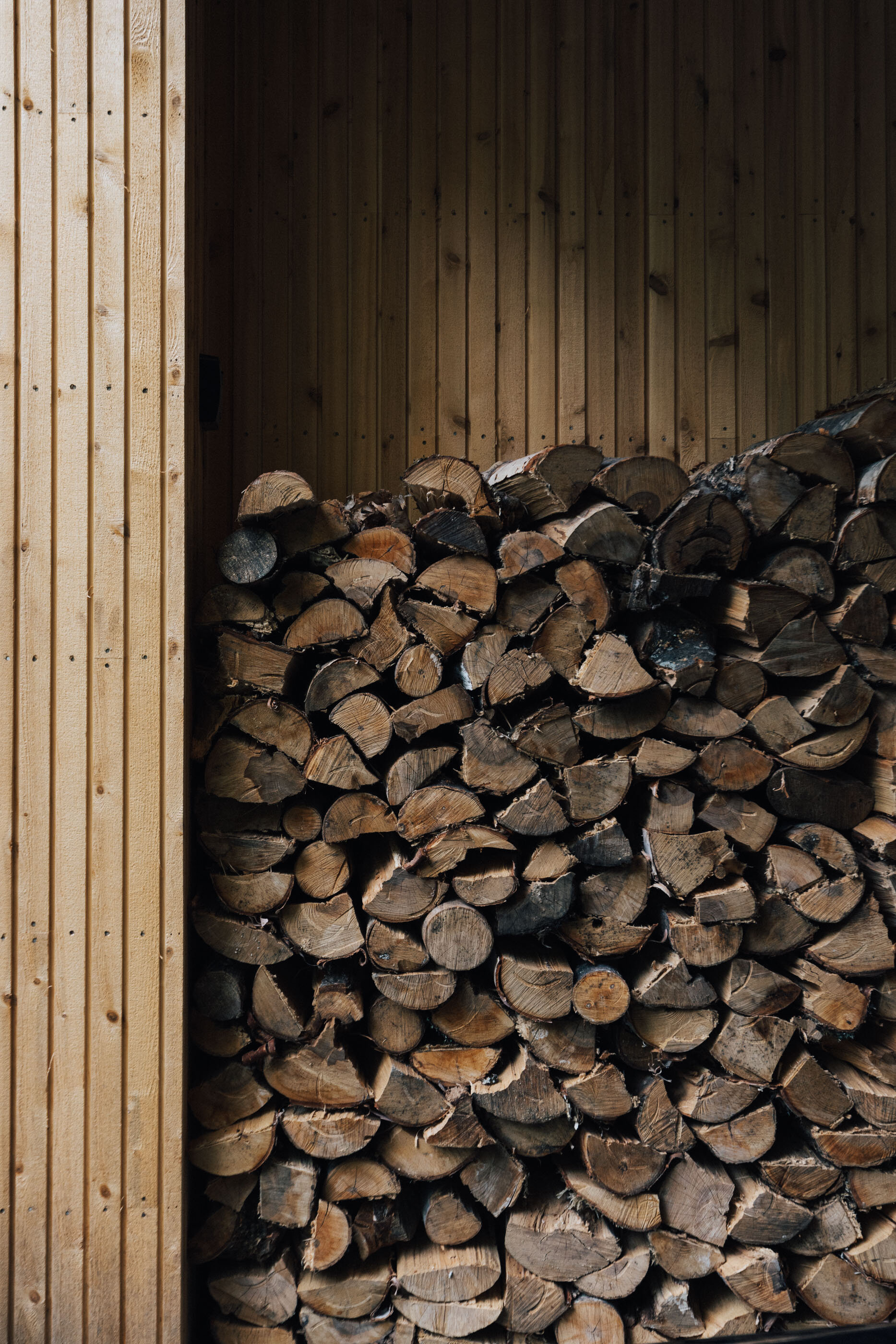 Stacked firewood against wood-paneled interior wall of a shed or cabin.