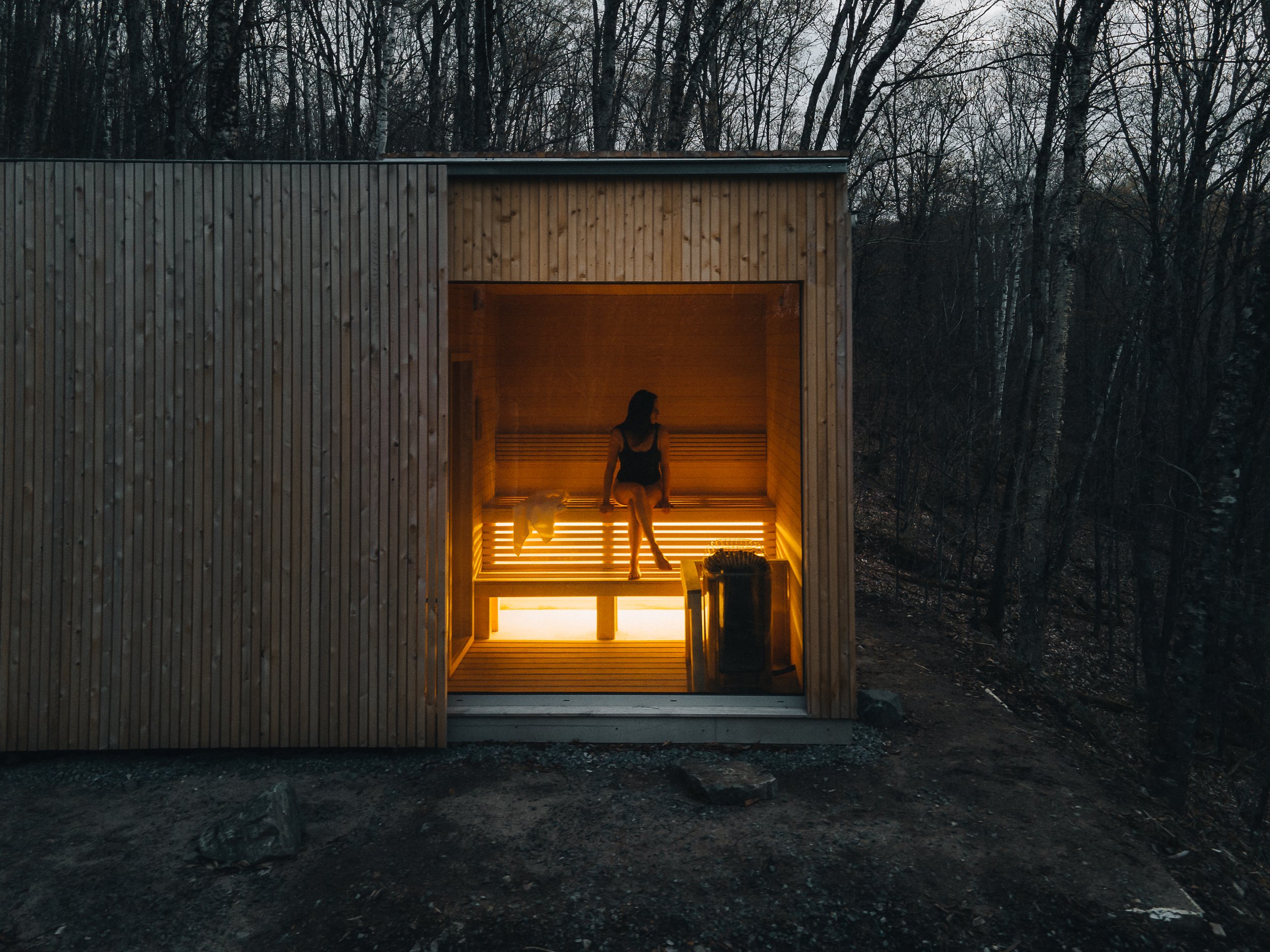 the hinterhouse sauna lit at dusk, set into the dark forest